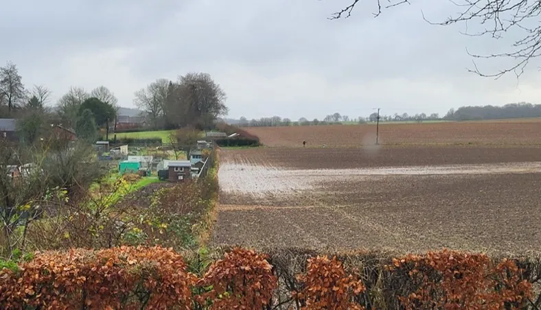 Floodwater lying across a ploughed field beside allotments